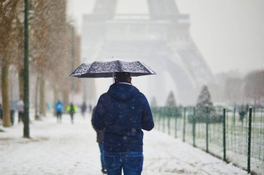 Paris 'teki Eyfel Kulesi' nin önünden geçen bir adam, yoğun kar yağışlı bir günde. Paris, Fransa 'da alışılmadık hava koşulları