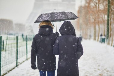Paris 'teki Eyfel Kulesi' nin önünden geçen çift, yoğun kar yağışlı bir günde. Paris, Fransa 'da alışılmadık hava koşulları. Kışın Fransa 'ya romantik bir gezi.