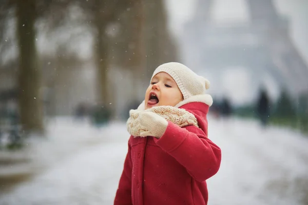 フランス パリのエッフェル塔の近くで舌で雪の結晶をキャッチ愛らしい幼児の女の子 雪と遊ぶ幸せな子供 子供のための冬の活動 — ストック写真