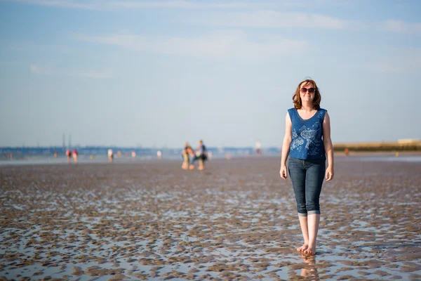 Schöne Frau, die bei Ebbe am Strand spaziert — Stockfoto