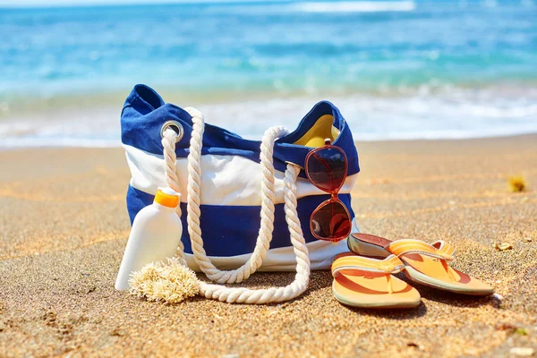 Beach bag, flip flops and sunscreen on beach — Stock Photo, Image