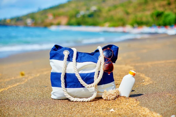 Bolsa de praia, chinelos e protetor solar na praia — Fotografia de Stock