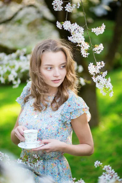 Девушка пьет чай в вишневом саду весной — стоковое фото