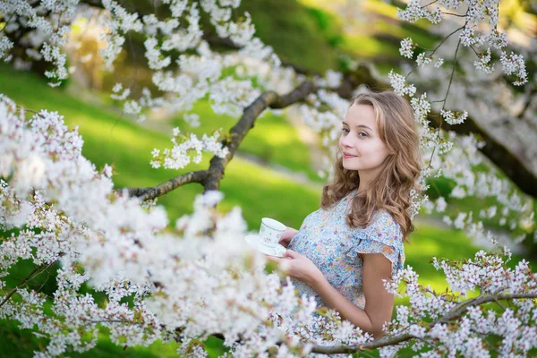 Menina bebendo chá no jardim de cereja em um dia de primavera — Fotografia de Stock