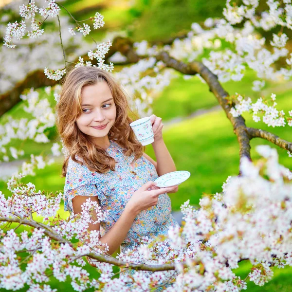 Woman in cherry blossom garden with cup of tea — Stock Photo, Image