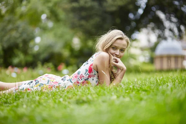 Ung flicka liggande i gräset på en sommardag — Stockfoto