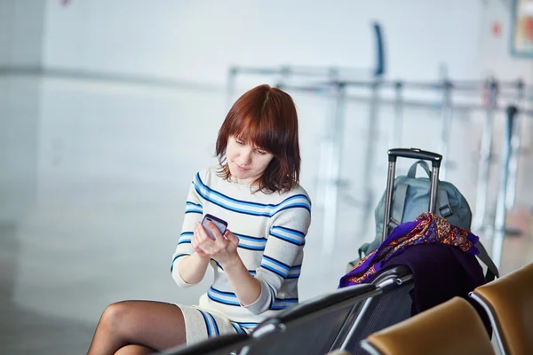 Young passenger at the airport, using her phone — Stock Photo, Image