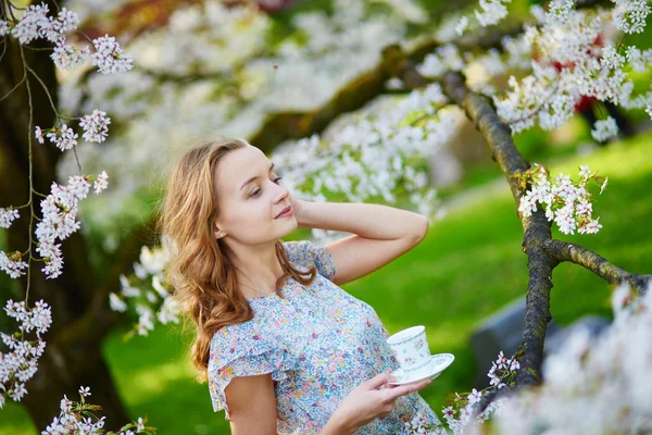 Jong meisje het drinken van thee in cherry tuin — Stockfoto