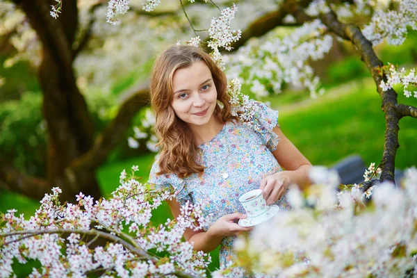 Mladá dívka pití čaje v třešňové zahrady — Stock fotografie