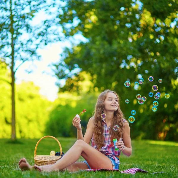 Girl sitting on the grass and blowing bubbles — Stock Photo, Image