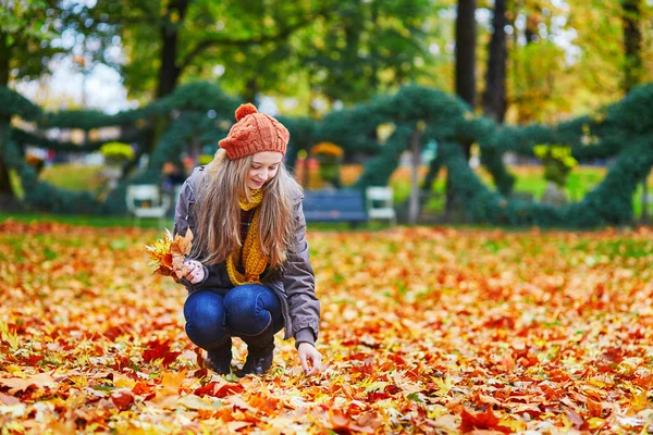Cheerful girl gathering autumn leaves in park — Stock Photo, Image
