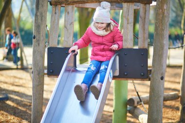 Sıcak kış kıyafetleri içindeki genç bir kız dışarıdaki tahta oyun parkına tırmanıyor ve dengede duruyor. Aktif çocukluk anı hareket, koordinasyon ve açık hava oyunlarına odaklandı