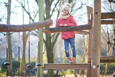Sıcak kış kıyafetleri içindeki genç bir kız dışarıdaki tahta oyun parkına tırmanıyor ve dengede duruyor. Aktif çocukluk anı hareket, koordinasyon ve açık hava oyunlarına odaklandı