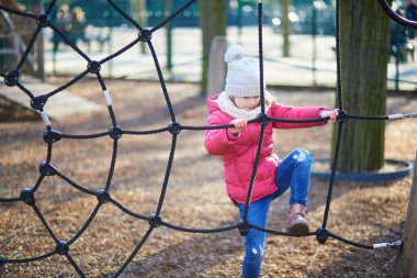 Sıcak kış kıyafetleri içindeki genç bir kız dışarıdaki tahta oyun parkına tırmanıyor ve dengede duruyor. Aktif çocukluk anı hareket, koordinasyon ve açık hava oyunlarına odaklandı