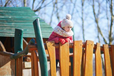 Sıcak kış kıyafetleri içindeki genç bir kız dışarıdaki tahta oyun parkına tırmanıyor ve dengede duruyor. Aktif çocukluk anı hareket, koordinasyon ve açık hava oyunlarına odaklandı