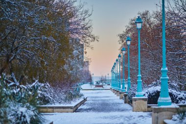 Paris 'in kış şehri. Gün doğumunda yakalanan sokak lambaları ve ağaçlarla kaplı karlı bir patika.