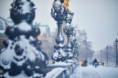 Paris 'te kar yağışı sırasında kar altında kalan Alexandre III köprüsü süslenmiş sokak lambaları ve altın heykeller manzaralı ve atmosferik şehir manzarası yaratıyor..