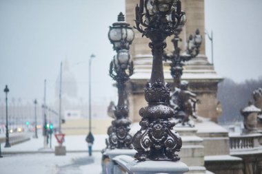 Paris 'te kar yağışı sırasında kar altında kalan Alexandre III köprüsü süslenmiş sokak lambaları ve altın heykeller manzaralı ve atmosferik şehir manzarası yaratıyor..