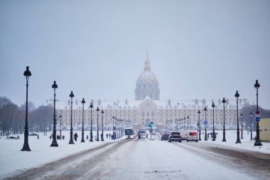 Karlı bir kış gününde Paris 'teki Les Invalides' in önü. Karla kaplı sokaklar, arabalar ve yayalar. Tarihi anıtın altın kubbesi, yumuşak gri gökyüzünün altında görülebilir..