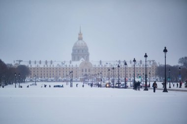 Karlı bir kış gününde Paris 'teki Les Invalides' in önü. Karla kaplı sokaklar, arabalar ve yayalar. Tarihi anıtın altın kubbesi, yumuşak gri gökyüzünün altında görülebilir..