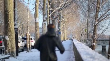Paris, Fransa - 6 Ocak 2026: Paris, Fransa 'da Seine nehri kıyısında karla kaplı bir kaldırım boyunca koşan bir kişinin dikiz görüntüsü. Çıplak ağaçlar, park etmiş arabalar ve arka planda görünen bir köprü..