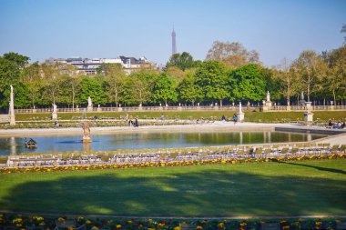 Paris, Fransa - 17 Mart 2025: Güneşli bir bahar gününde Paris 'teki Jardin du Lüksemburg' daki merkez çeşmenin etrafında dinlenen kalabalık, arka planda Eyfel Kulesi ile birlikte.