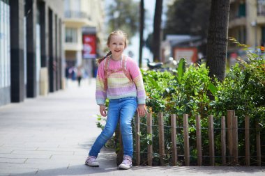 Renkli bir kazak ve sırt çantası giymiş gülümseyen genç kız güneşli bir günde şehir caddesinde yürüyor..