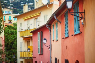 Akdeniz kıyısındaki bir kasabada mavi panjurları ve ulusal bayrakları olan renkli binaların canlı görüntüsü.
