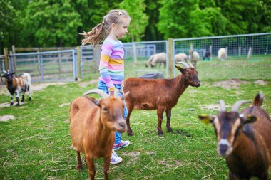 Evcil hayvan ya da çiftlikte keçiye bakarken çömelmiş gülümseyen küçük kız..
