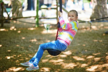 Küçük kız yeşil bir şehir parkındaki oyun parkında teleferik yolculuğunun tadını çıkarıyor. Çocuk dışarıda oynuyor, aktif oyun sırasında denge, güç ve koordinasyon geliştiriyor.