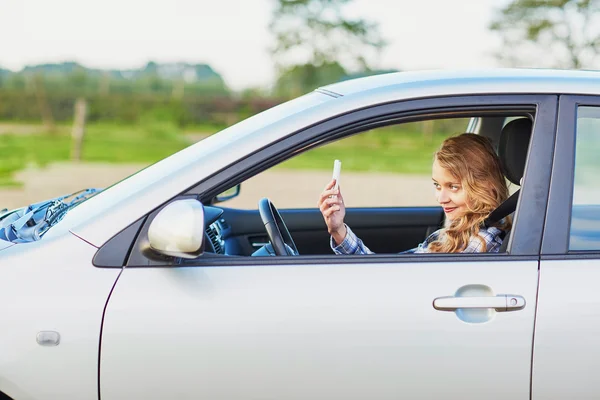 Jonge vrouw rijden een auto en het gebruik van de telefoon — Stockfoto