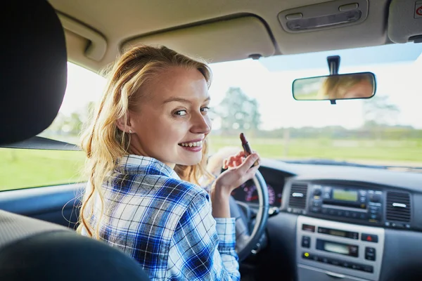 Woman applying lipstick in a car while driving — Stock Photo, Image