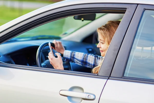 Jonge vrouw rijden een auto en het gebruik van de telefoon — Stockfoto