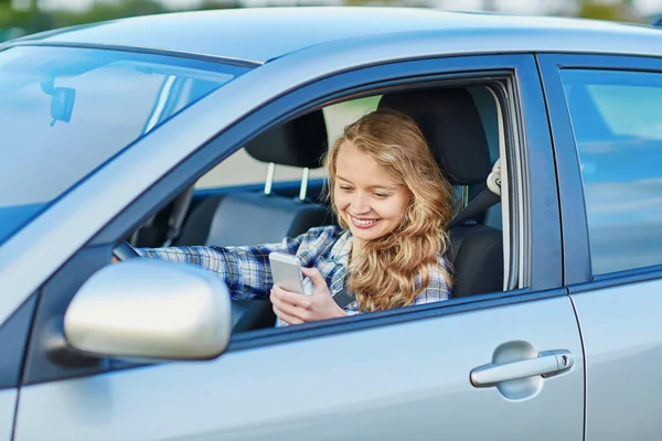 Молодая женщина за рулем автомобиля и с помощью телефона — стоковое фото
