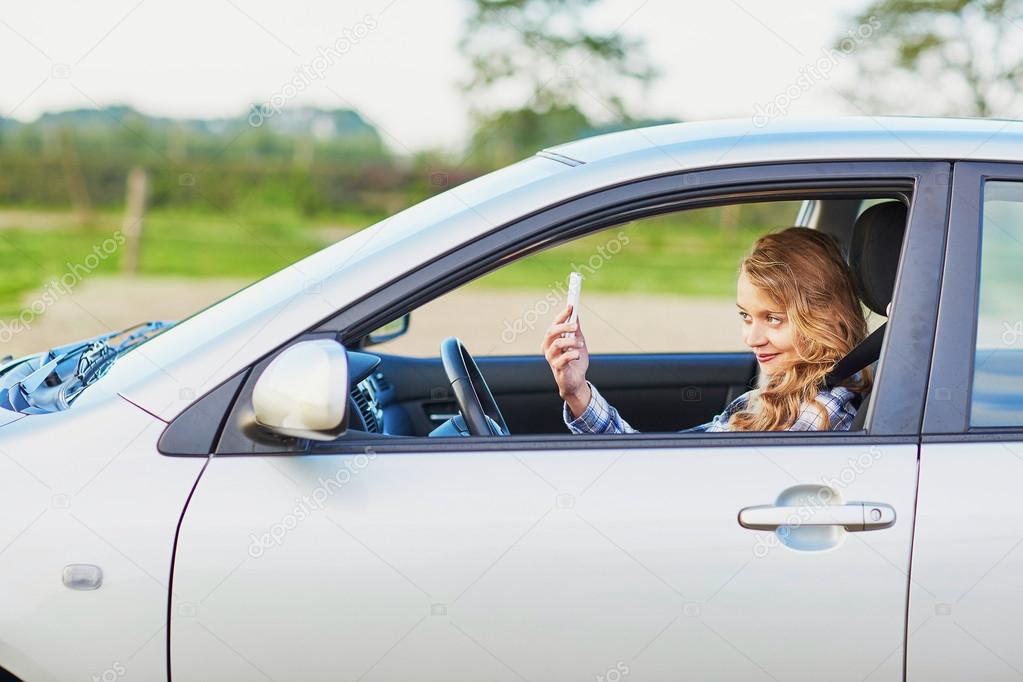 young woman driving a car and using phone