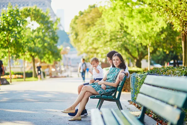 Glad familj på tre sitter på bänken nära Eiffeltornet — Stockfoto