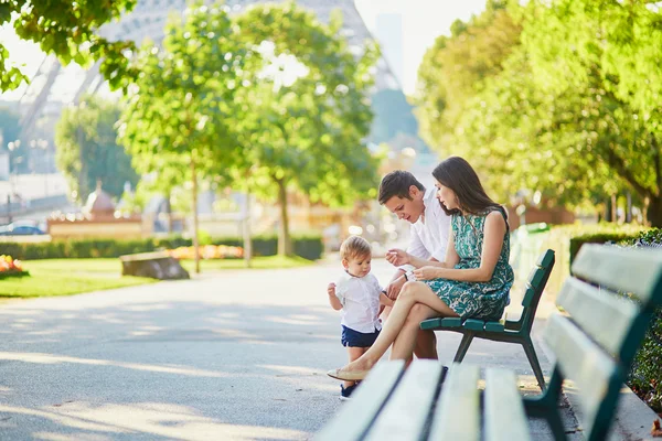 Счастливая семья из трех человек сидит на скамейке возле Эйфелевой башни — стоковое фото