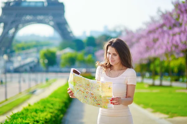 Молодая женщина у Эйфелевой башни в Париже, глядя на карту города — стоковое фото