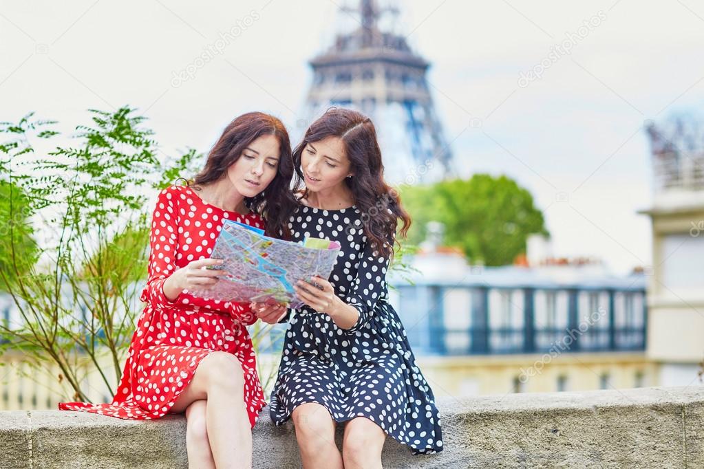 Beautiful twin sisters using map in front of Eiffel Tower