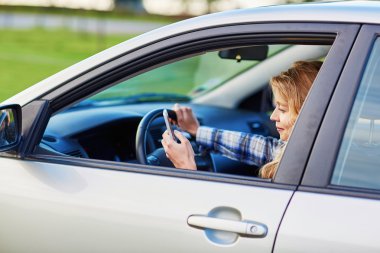 Woman using her smartphone while driving a car clipart