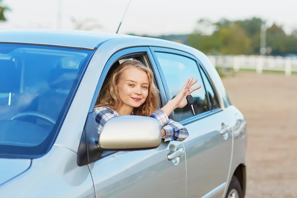 Motorista jovem olhando para fora da janela do carro segurando uma chave — Fotografia de Stock