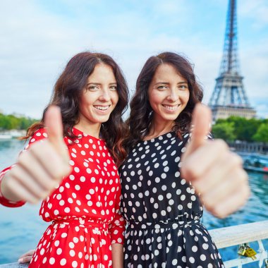Eyfel Kulesi önünde başparmak gösterilmesini neşeli gülümseyen ikiz kız Paris