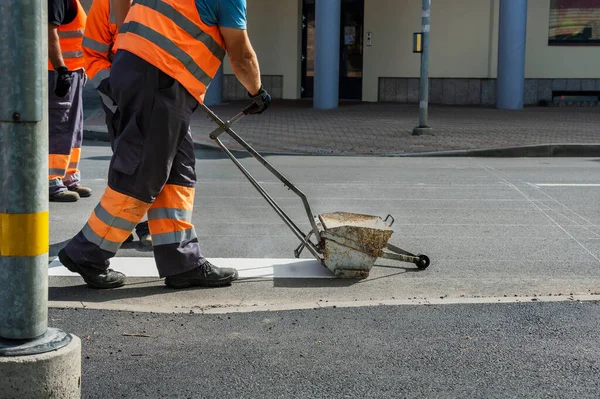 Men works on the road, painting white lines of crosswalk.