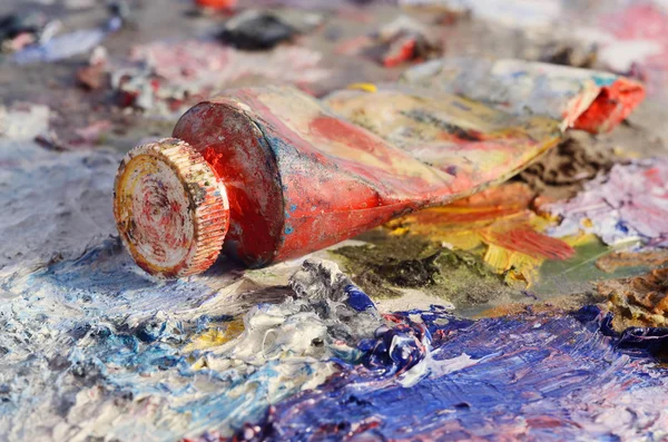 Closeup of old oil paint tube with red colour lying on dirty artistic palette ,background for creative art design