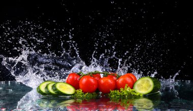 Stüdyo ile vurdu freeze hareket kiraz domates ve siyah arka plan üzerine su sıçrama içinde salatalık dilimleri