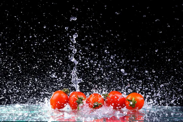 Studio schoot met bevriezen motie van cherry tomaten in water splash op zwarte achtergrond met kopie ruimte — Stockfoto