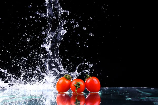 Studio shot with freeze motion of cherry tomatoes in water splash on black background with copy space — Stock Photo, Image