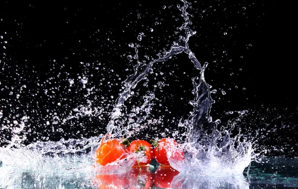 Studioaufnahme mit Gefrierbewegung von Kirschtomaten im Wasserspritzer auf schwarzem Hintergrund mit Kopierraum — Stockfoto