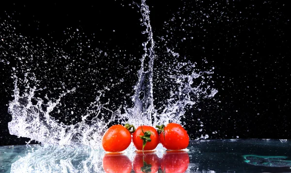 Studio shot with freeze motion of cherry tomatoes in water splash on black background with copy space — Stock Photo, Image