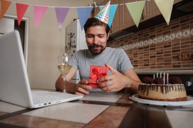 Karantina zamanında doğum gününü kutlayan bir adam. Coronavirus salgını 2020. Adam kutuyu açıyor ve hediyeyle çok mutlu oluyor. Arkadaşlarla uzaktan iletişim kurmak.